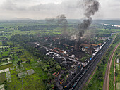 Luftaufnahme einer rauchenden Fabrik vor einer Kulisse aus üppigem Grün und Eisenbahnschienen, die Industrie und Natur gegenüberstellt, Chandil, Jharkhand, Indien.