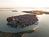 Aerial view of sun-kissed island with tightly packed houses, boasting a vibrant palette of colors, and a prominent church tower soaring above, Burano, Veneto, Italy.