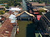 Aerial view of the iconic Damnoen Saduak floating market's bustling canal, with boats navigating under aged wooden bridges amidst vibrant shops, Damnoen Saduak, Thailand.