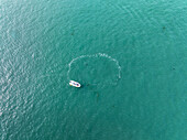 Aerial view of a lone boat adrift in the vast expanse of the ocean, its wake painting ephemeral arcs on the turquoise canvas, Bernières-sur-Mer, Normandy, France.