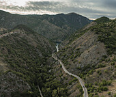 Aerial view of a winding road carving through rugged, verdant mountains, contrasting with the muted sky above, Scanno, Abruzzo, Italy.