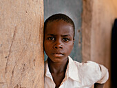Katsina, Nigeria - 17 July 2024: View of a young boy's earnest gaze against a textured wall, his white shirt a stark contrast to the earth-toned backdrop.