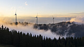Aerial view of wind turbines standing proudly above a sea of clouds, their sleek forms contrasting with the rugged, forested hills, Gaberl, Styria, Austria.