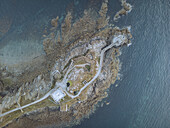 Aerial view of the weathered Kermorvan Fort and lighthouse standing against the turbulent, deep blue sea, connected by a narrow causeway, Le Conquet, Bretagne, France.