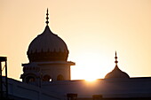 View of the Gurdwara bathed in the golden hues of the setting sun, its domes silhouetted against the sky in Kartarpur, Punjab, Pakistan.