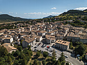 Luftaufnahme der malerischen Stadt inmitten sanfter Hügel, mit der belebten Piazza unter den alten Kirchtürmen, Pescocostanzo, Abruzzen, Italien.