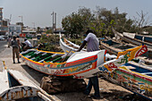 Dakar, Senegal - 12 May 2025: View of colorfully adorned boats resting near Plage de Soumbédioune, where artisans meticulously work, blending tradition with the vibrant pulse of Senegalese life.