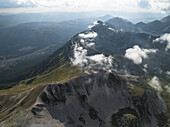 Luftaufnahme von zerklüfteten Gipfeln, die den Himmel durchdringen, deren felsige Gesichter von Wolkenfetzen aufgeweicht werden, ein Tanz von Licht und Schatten über dem Gran Sasso-Gebirge, Campo Imperatore, Abruzzen, Italien.