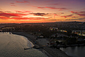 Luftaufnahme der Küste und des Hafens im warmen Licht der untergehenden Sonne, während der Himmel von feurigem Rot in sanfte Orangetöne übergeht, Dana Point, Kalifornien, Vereinigte Staaten.