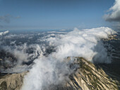 Luftaufnahme von Wolken, die um die Berggipfel wirbeln und einen dramatischen Kontrast zum klaren Himmel bilden, Gran Sasso, Abruzzen, Italien.