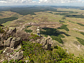 Aerial view of a lone figure standing atop rocky terrain, gazing over the vast, green expanse of Chiricayen Tepui, Santa Elena de Uairen, Venezuela.