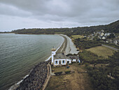 Aerial view of The Phare de Nantouar lighthouse with blue trim standing sentinel against the grey Atlantic, where land meets sea, Louannec, Bretagne, France.