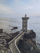 Aerial view of the Kermorvan lighthouse standing tall against the crashing waves, a beacon of light against the muted sky, Le Conquet, Bretagne, France.