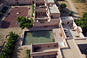 Nagaur, Indien - 19. Oktober 2010: Luftaufnahme eines rustikalen Palastes, dessen Sandsteinmauern in der Sonne glühen und sich in dem ruhigen, von geometrischen Höfen umgebenen Pool spiegeln.