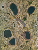 Luftaufnahme einer Ansammlung von dunklen, stillen Seen inmitten der trockenen, sonnenverbrannten Landschaft, deren Oberflächen den Himmel über ihnen spiegeln, Aaqoura, Libanon, Libanon, Bergland.