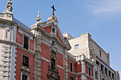 Blick auf ein Gebäude mit einem Kreuz auf dem Dach mit roten und weißen Wänden und blauem Himmel darüber, Madrid, Spanien.