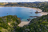 Luftaufnahme der ruhigen Bucht mit Sandstrand, umrahmt von üppigen grünen Hügeln und dem ruhigen Ozean, Matapouri Bay, Matapouri, Te Tai-tokerau, Neuseeland.