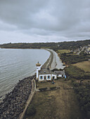 Aerial view of The Phare de Nantouar lighthouse with its contrasting dark roof perched on the rocky coast, where the ocean meets the land, Louannec, Bretagne, France.