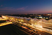 Luftaufnahme der wellenförmigen, beleuchteten Struktur der Stazione AV Mediopadana, ein Leuchtturm der modernen Architektur in der Dämmerung, Stazione AV Mediopadana, Emilia-Romagna, Italien.