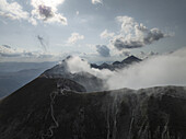Luftaufnahme von zerklüfteten, in ätherischen Nebel gehüllten Gipfeln, die in starkem Kontrast zur zerklüfteten Landschaft darunter stehen, Gran Sasso, Abruzzen, Italien.