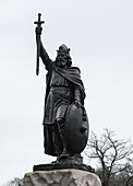 Blick auf eine Bronzestatue von König Alfred dem Großen, der stolz vor einem blassen Winterhimmel steht und ein Schwert und einen Schild hält, Winchester, England, Vereinigtes Königreich.