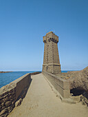 View of the Phare de Mean Ruz standing proudly against the azure sky, connected by a stone pathway over turquoise waters, Perros-Guirec, Brittany, France.