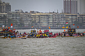 Mumbai, India - 07 September 2025: View of vibrant boats, adorned with flags and filled with devotees, carrying the idol through the grey waters near the Marine Drive buildings.