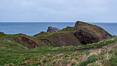 View of rugged coastline where the grassy cliffs meet the moody blue sea under an overcast sky, a tranquil scene of natural beauty, Cullen, Scotland, United Kingdom.