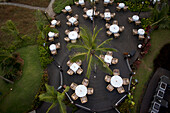 Bambolim, India - 17 November 2013: Aerial view of a circular outdoor dining area, tables draped in white linen nestled amidst lush greenery and palm trees.