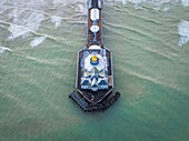 Luftaufnahme des Piers von Eastbourne, der ins Meer ragt und dessen verschnörkelte weiß-blaue Struktur mit dem türkisfarbenen Wasser und den schäumenden Wellen kontrastiert, Eastbourne, Vereinigtes Königreich.