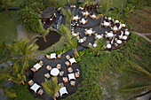 Bambolim, India - 16 November 2013: Aerial view of a meticulously arranged outdoor dining area, where tables with white linens are nestled amidst lush greenery and swaying palm trees.