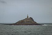 View of the small rocky island with a building on top stands solitary against the grey sea and sky, a beacon of history and nature, ilot Saint-Michel, Bretagne, France.