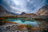View of a serene turquoise lake mirroring the rugged mountains under a dramatic sky, a blend of nature's raw power and serene beauty, Hunza Nagar, Gilgit Baltistan, Pakistan.