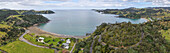 Luftaufnahme der ruhigen Bucht, wo die kurvenreiche Straße durch üppig grüne Hügel zum ruhigen Wasser führt, Helena Bay, Northland, Neuseeland.