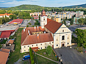 Aerial view of the historic church with its terracotta roof and adjacent buildings casting shadows on the pavement, Filakovo, Banská Bystrica Region, Slovakia.