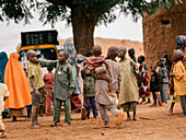 Katsina, Nigeria - 17. Juli 2024: Blick auf Kinder, die sich in einem sonnenüberfluteten, erdfarbenen Dorf versammeln. Der ockerfarbene Boden steht im Kontrast zu den gedämpften Farben der traditionellen Gebäude.