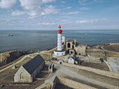 Aerial view of the Pointe Saint-Mathieu Lighthouse, with its striking red and white tower, stands majestically amidst ancient ruins overlooking the serene sea, Plougonvelin, Bretagne, France.