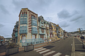 Blick auf farbenfrohe, historische Villen am Strand, die sich stolz gegen den bedeckten Himmel abheben und deren verzierte Fassaden das reiche Erbe der Stadt widerspiegeln, Mers-les-Bains, Hauts-de-France, Frankreich.
