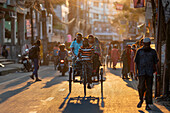 Bogura, Bangladesh - 16 October 2022: View of a vibrant street scene bathed in the warm glow of the setting sun, with rickshaws and pedestrians moving along the bustling road.