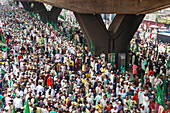 Chattogram, Bangladesh - 08 October 2022: View of a dense crowd of people, many holding green flags, filling the street beneath a concrete overpass, a sea of faces in a vibrant display of unity.
