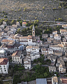 Aerial view of a compact village nestled against a rugged mountainside, with the church spire rising above the terracotta rooftops, Rocca Calascio, Abruzzo, Italy.