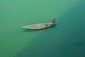 Rangpur, Bangladesch - 30. November 2019: Luftaufnahme einer einsamen Gestalt in einem verwitterten Holzboot, die über das ruhige Wasser gleitet, eine friedliche Szene, in der Licht und Schatten auf der Oberfläche des Flusses tanzen.