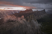 Aerial view of jagged peaks piercing through ethereal mists under a dramatic, sun-kissed sky, revealing the raw beauty of the Dolomites, Cortina d'Ampezzo, Veneto, Italy.