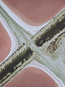 Aerial view of the stark geometric lines bisecting the vibrant pink salt flats along Route du Grau du Roi, Aigues-Mortes, Occitanie, France.