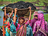 Dhaka, Bangladesh - 17 March 2017: View of women carrying headloads of coal, their vibrant saris contrasting against the gritty darkness of their burdens.