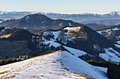 Aerial view of snow-dusted peaks rise against a backdrop of distant, hazy mountains, a cross standing prominently, Sommeralm, Steiermark, Austria.