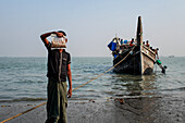 Cox's Bazar, Bangladesh - 07 March 2022: View of a young boy holding a translucent bag, with a traditional fishing boat in the tranquil, sun-kissed sea, creating a serene yet poignant scene.