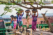 Dhaka, Bangladesh - 14 May 2023: View of women balancing baskets of coal on their heads, creating a striking contrast against the river and sky.