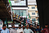 Chattogram, Bangladesh - 08 October 2022: View of a gathering of people with green flags, some on a pedestrian overpass, under a modern building facade.