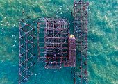 Aerial view of the skeletal remains of the West Pier jutting out into the sea, with turquoise water contrasting against the rusted metal structure, Brighton and Hove, England, United Kingdom.